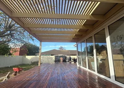 Timber slat pergola over a hardwood deck beside a glass-walled living area